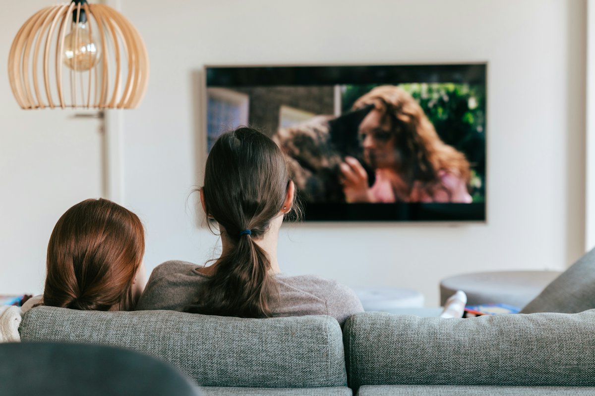 Két ember a kanapén, falra szerelt televíziót néznek